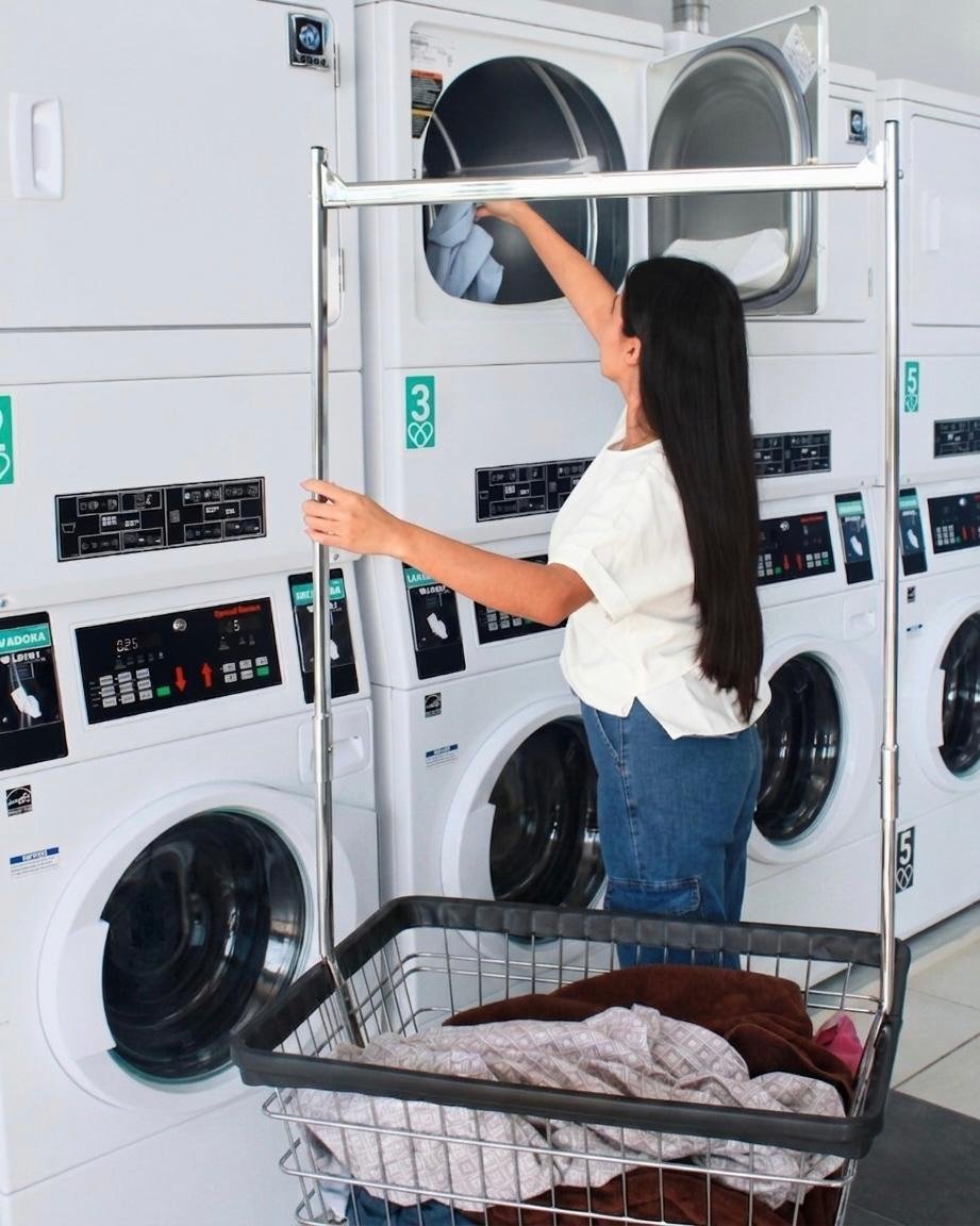 Woman loading clothes into a commercial dryer at a laundromat with a laundry basket below